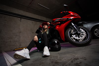 Wearing a black jacket and black pants women sitting on red sports cars
